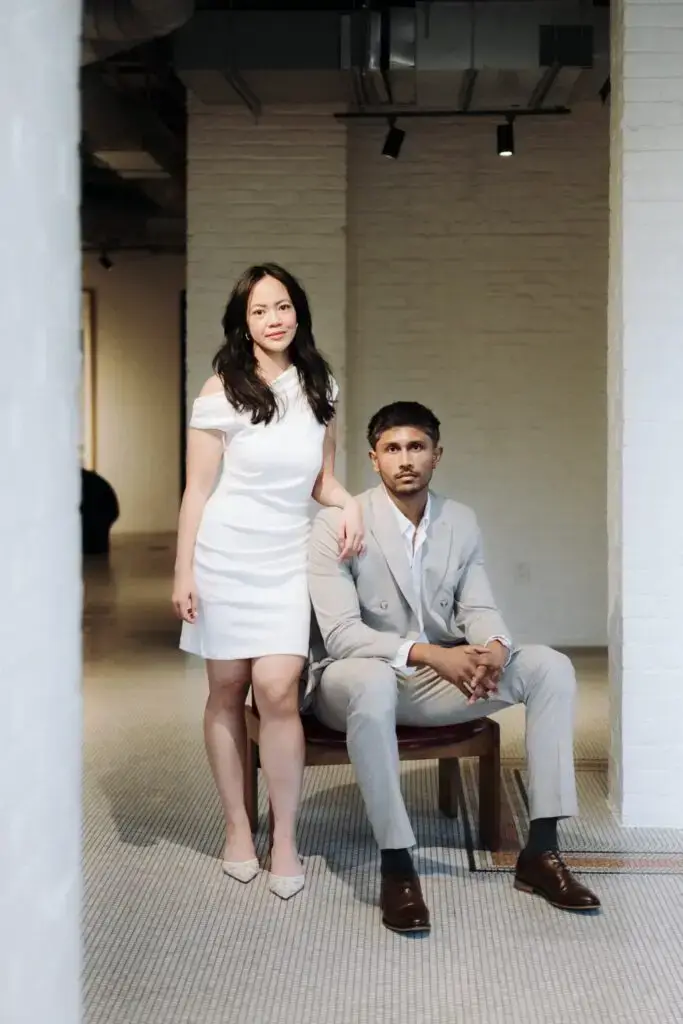 Grace standing beside Neel, seated in a lounge chair